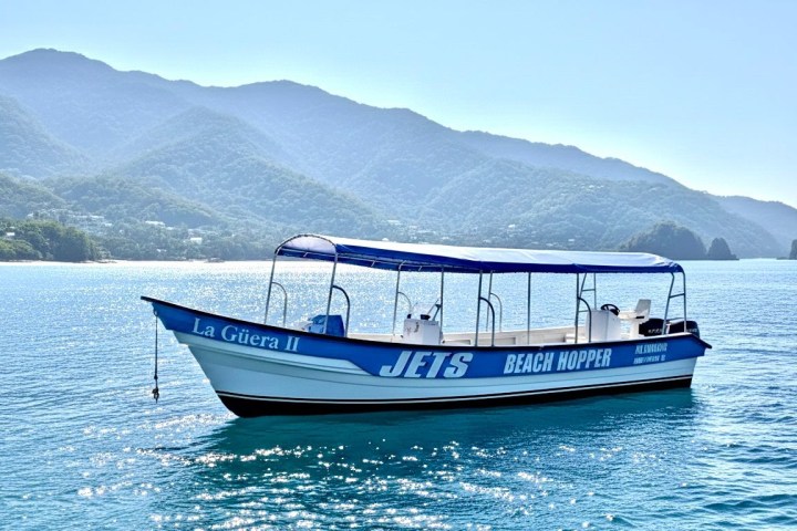 Small tour boat named 'Jets Beach Hopper' on calm water with mountains in background.