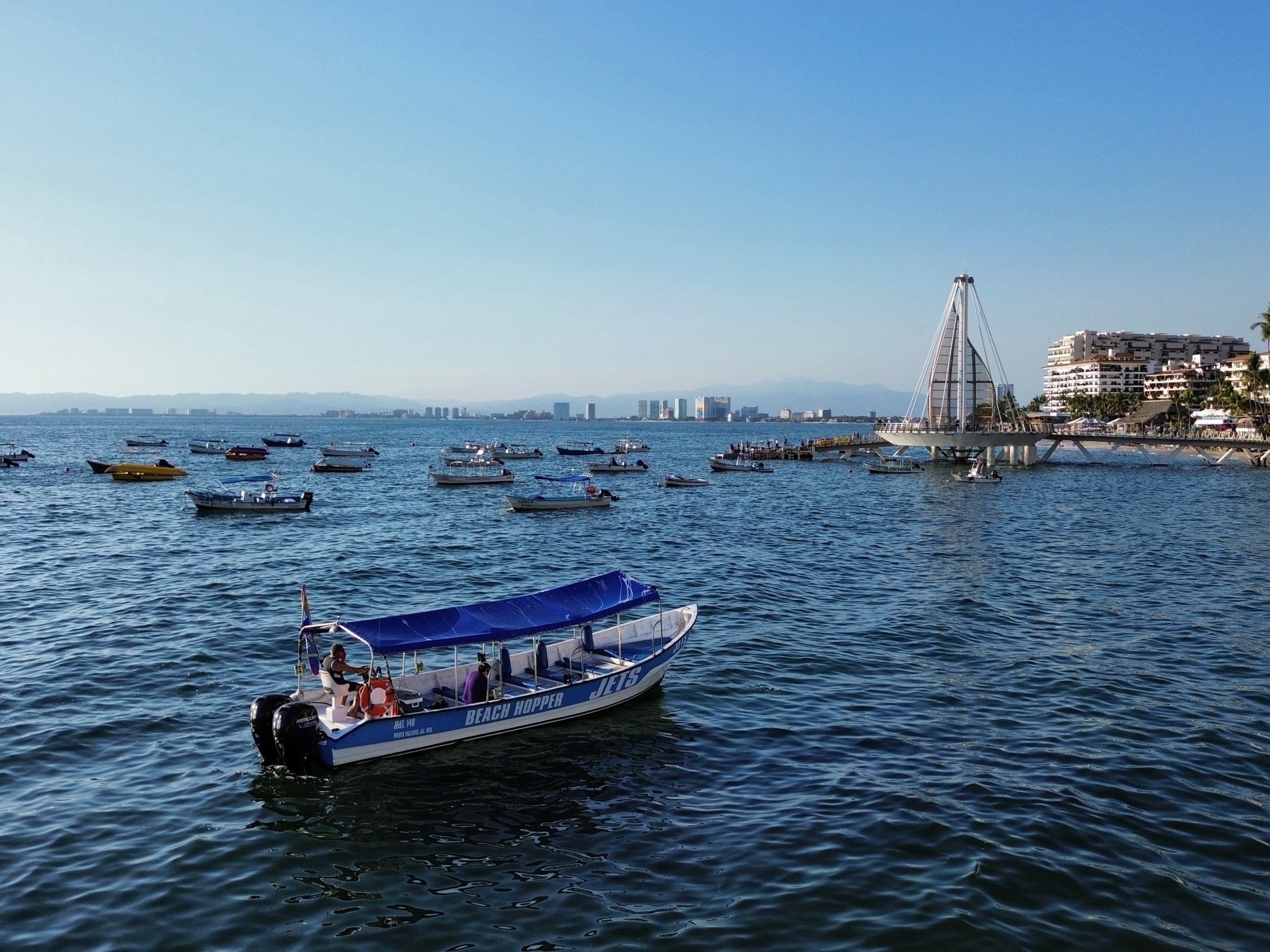 Small boats on the ocean near a coastal city with a dock and modern structure.
