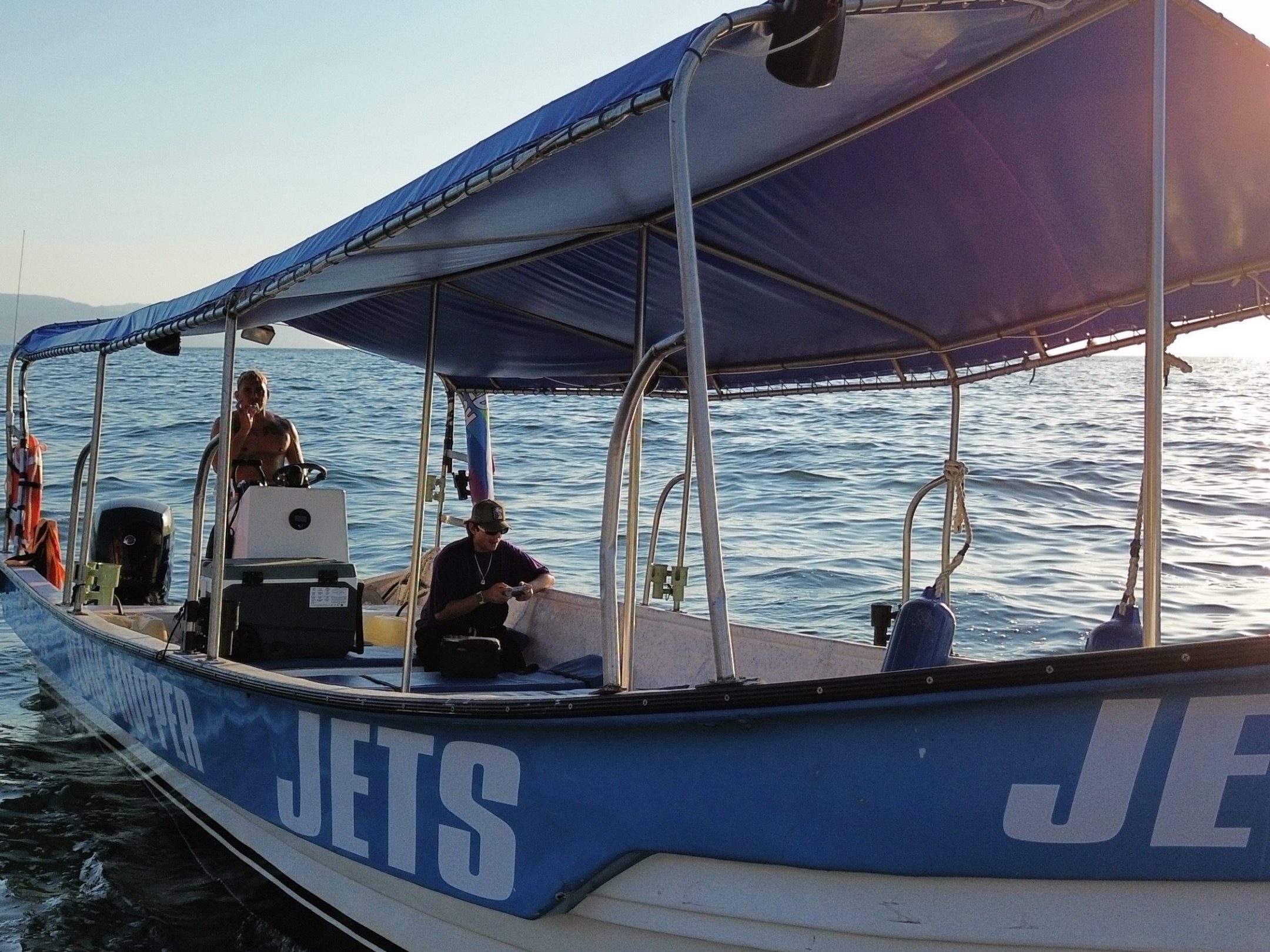 People on a blue and white boat near the sea at sunset.