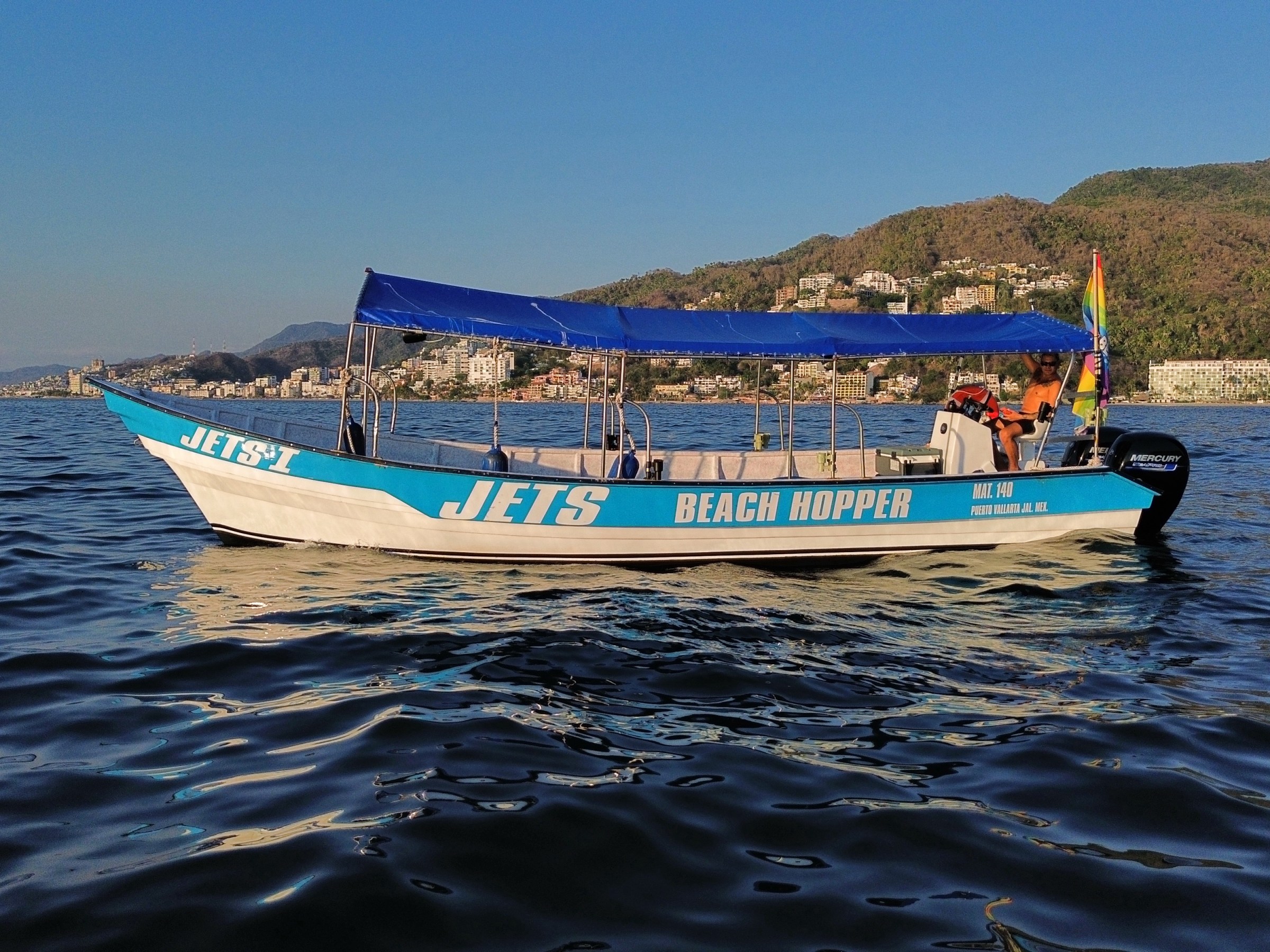 Boat named JETS BEACH HOPPER on calm water with hills in background.