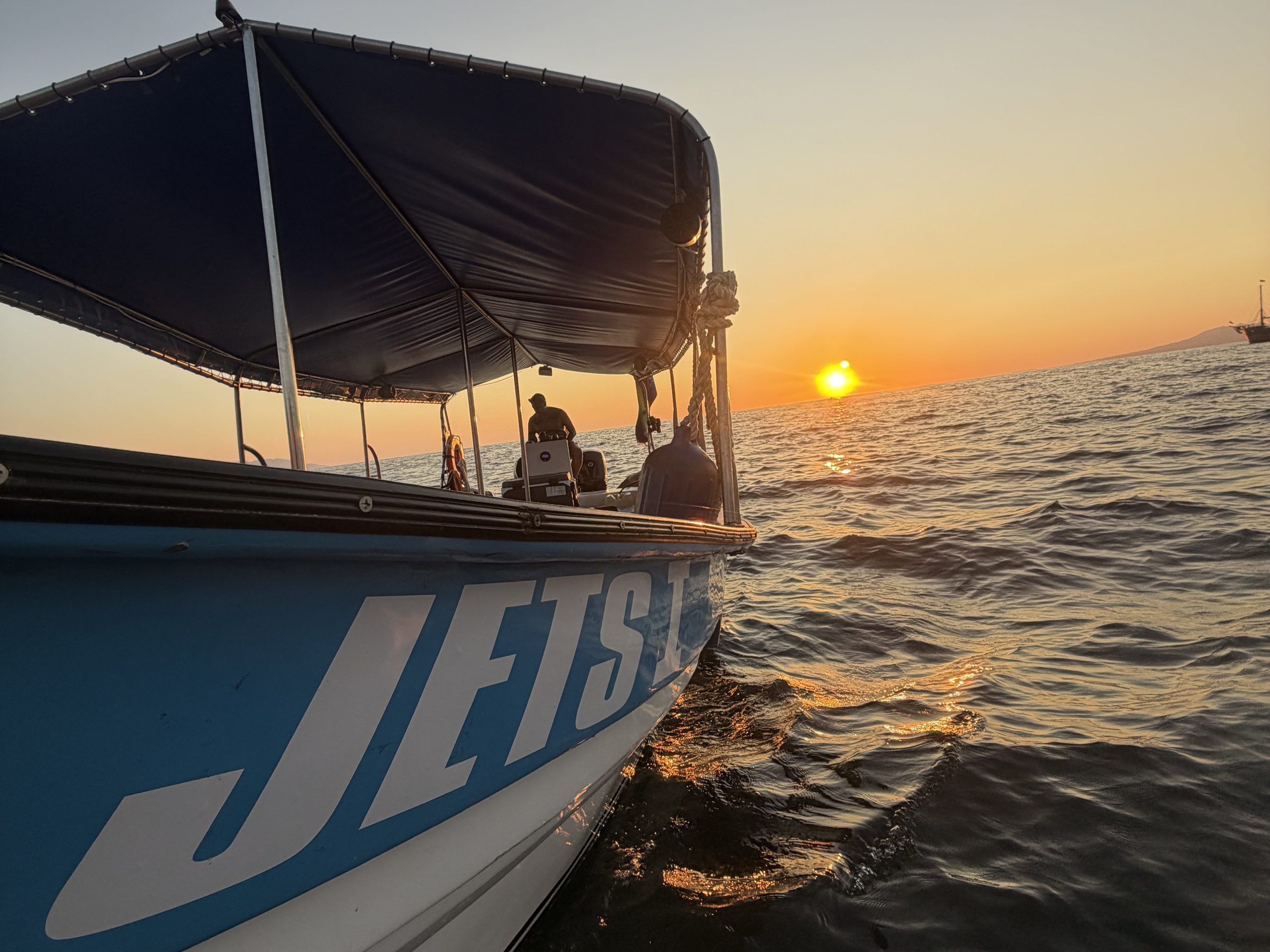 Boat on water at sunset with visible waves and orange sky.