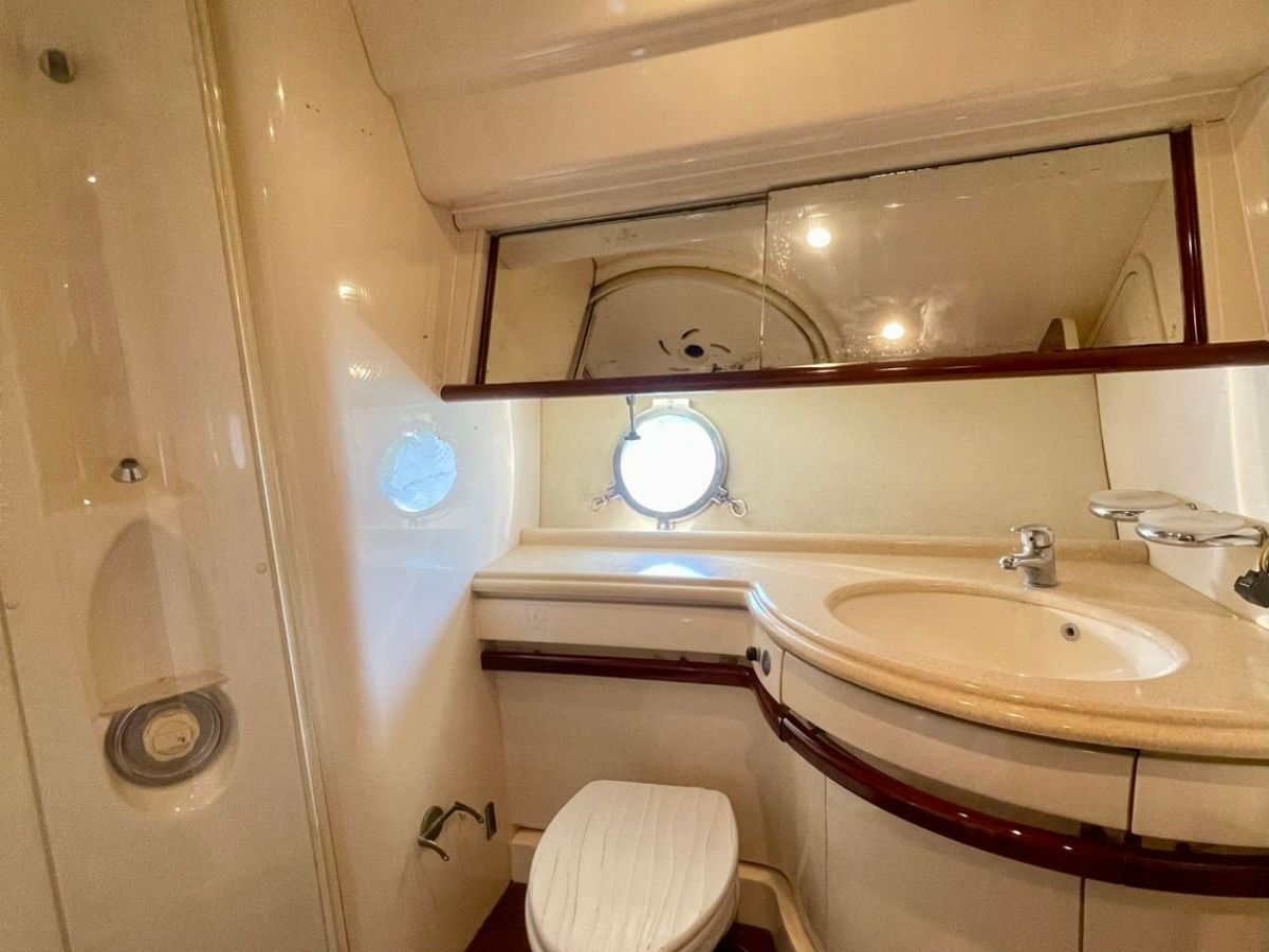 Compact boat bathroom with toilet, sink, and round window.