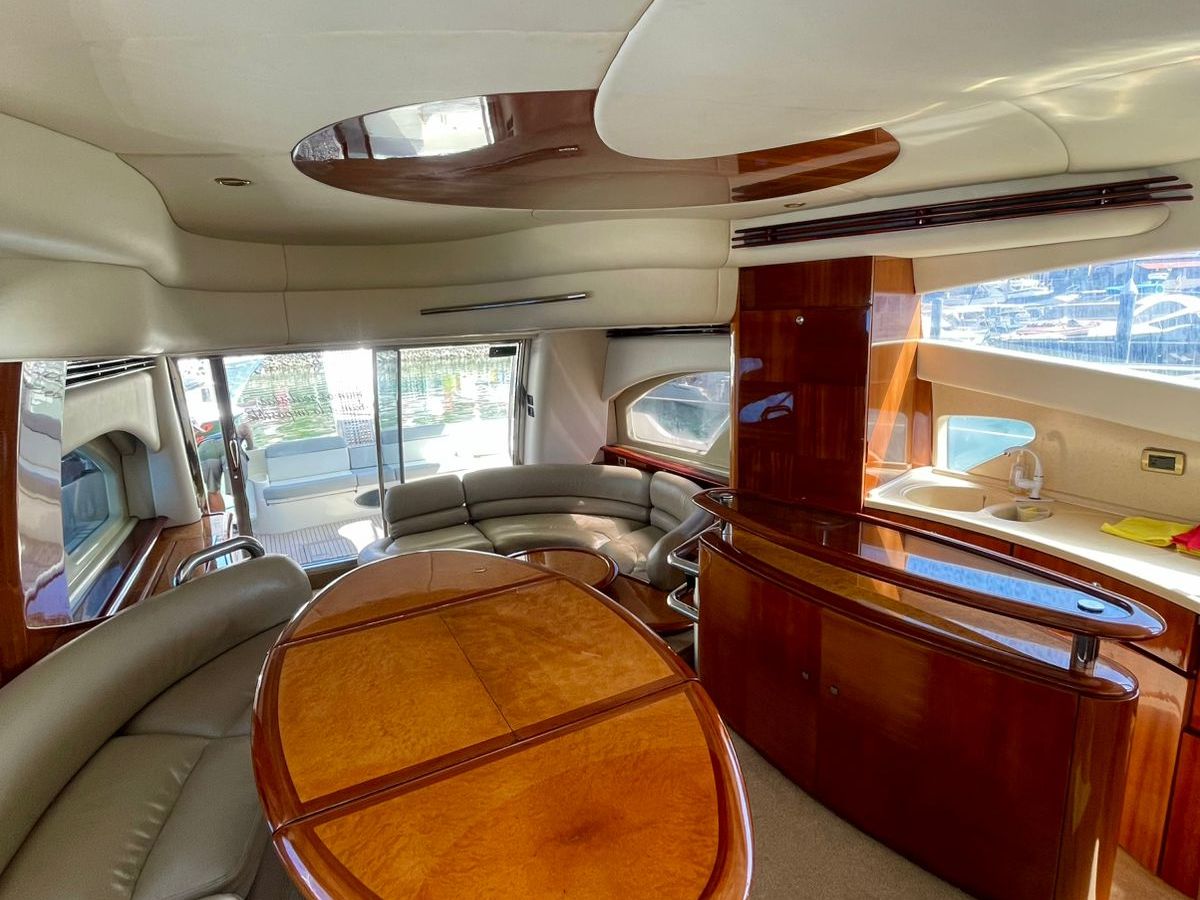Luxurious yacht interior with curved seating, wooden table, and windows overlooking water.
