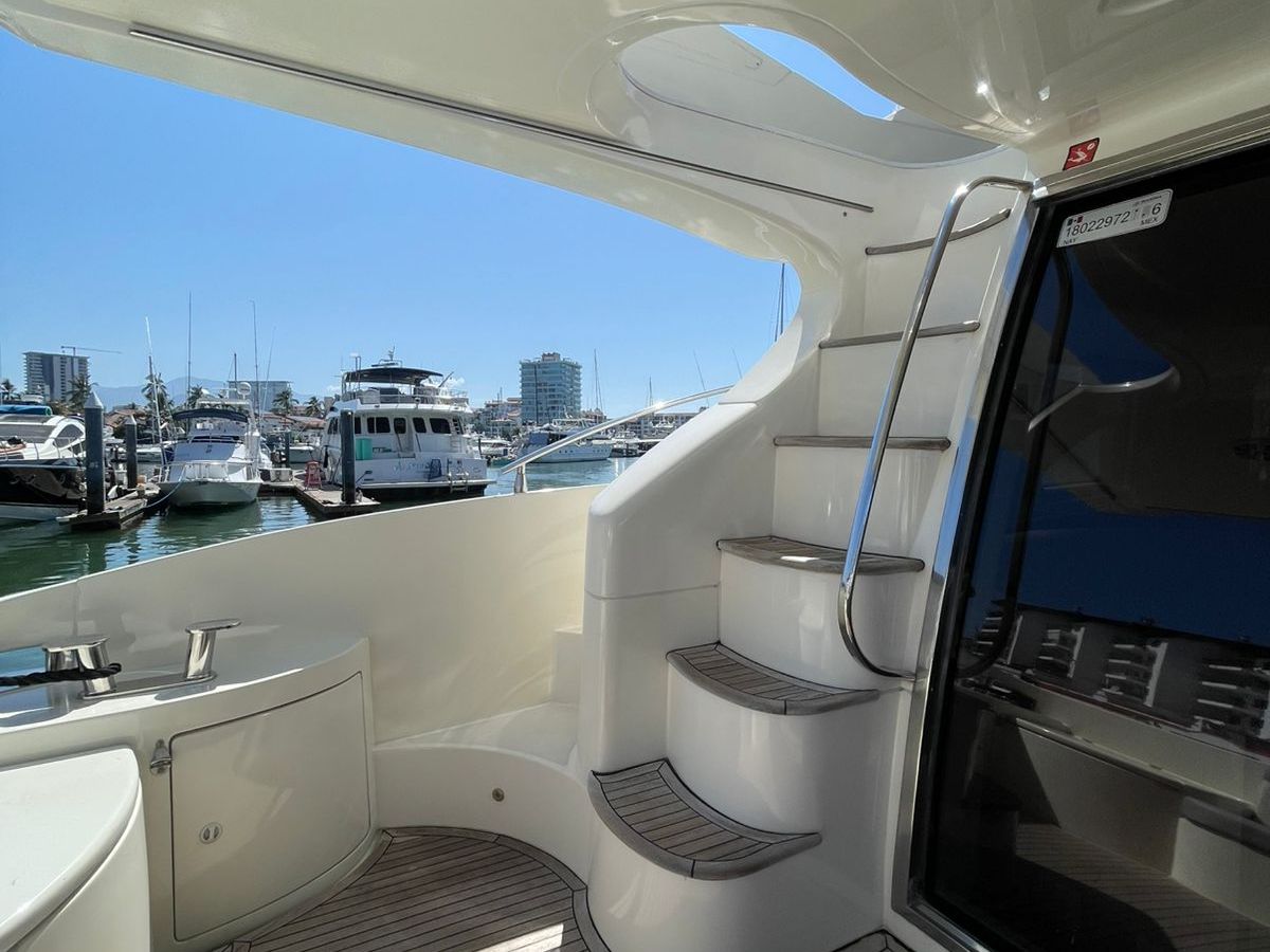 View from a yacht's deck with spiral stairs, overlooking a marina with boats on a sunny day.