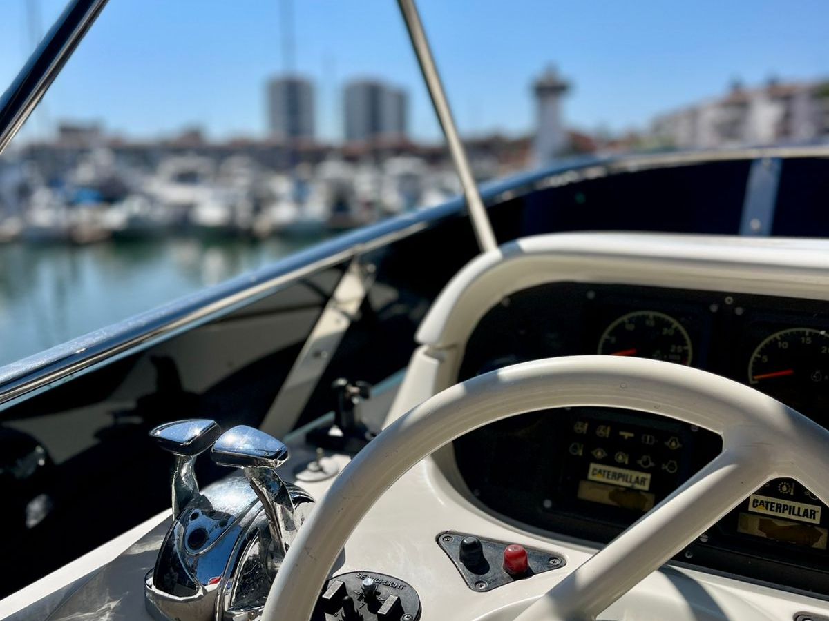 Boat helm with steering wheel and marina view on a clear day.
