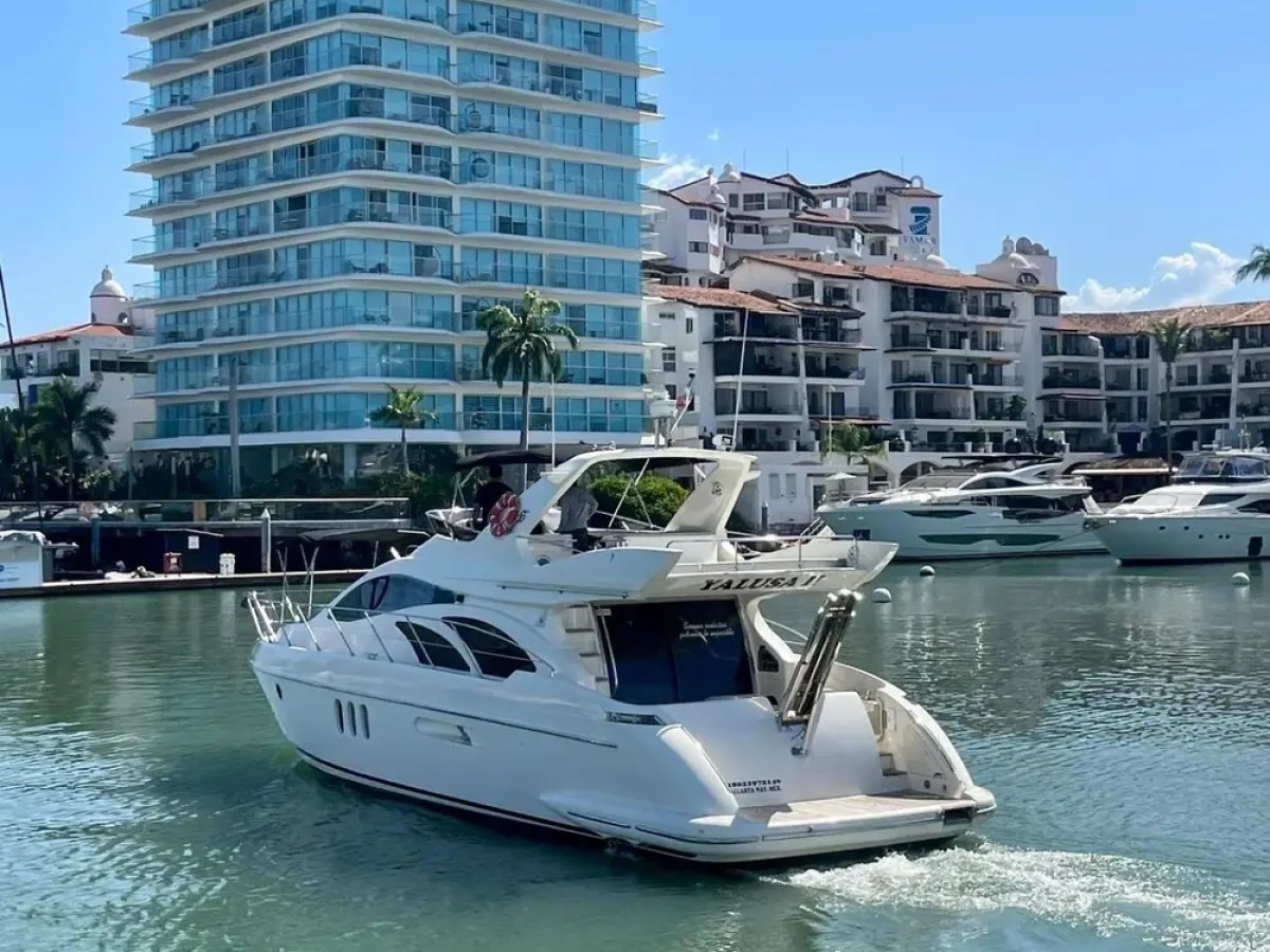 White yacht in marina with modern high-rise and palm trees in background.