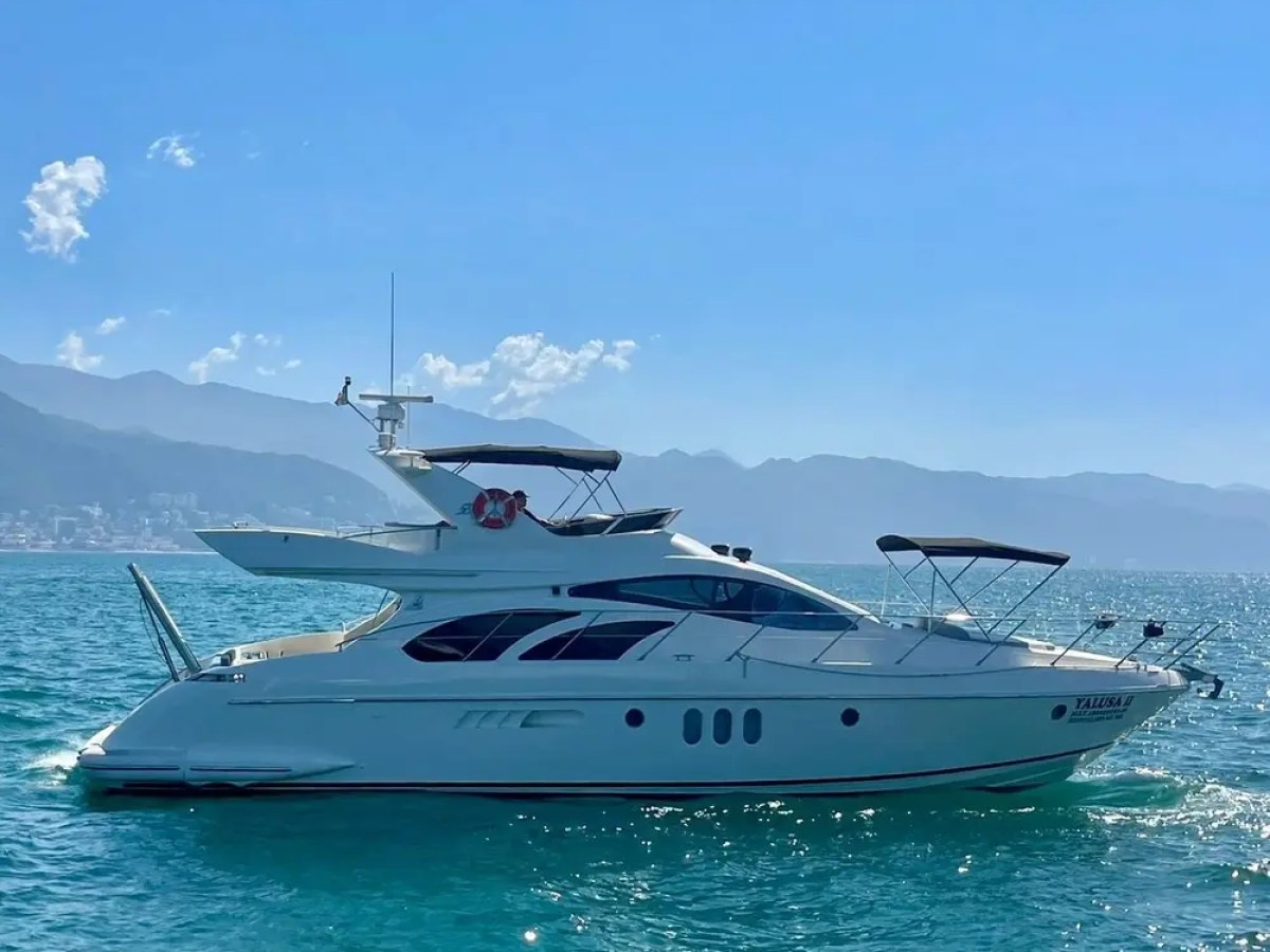 White yacht on calm blue sea with mountains in the background.
