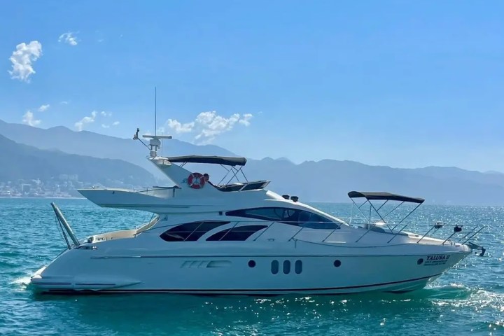 White yacht on calm blue sea with mountains in the background.
