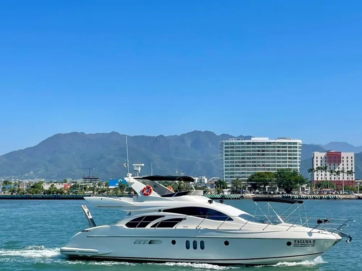 White yacht on water with city and mountains in background under clear blue sky.