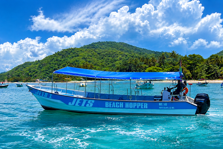 Boat with blue canopy named 'JETS BEACH HOPPER' on clear water near lush green hills.