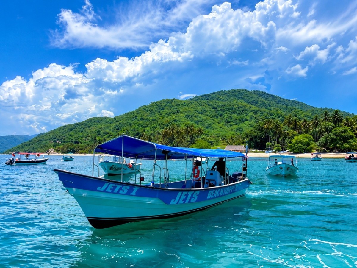 Boat on turquoise water near a tropical island under a cloudy sky.