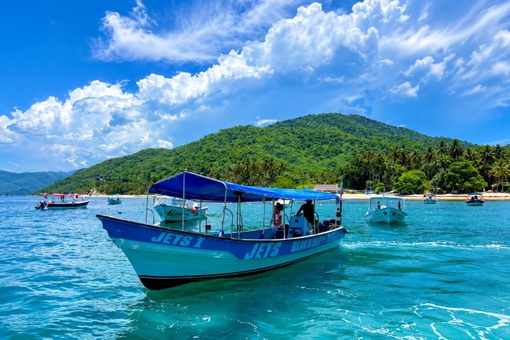 Boat on turquoise water near a tropical island under a cloudy sky.