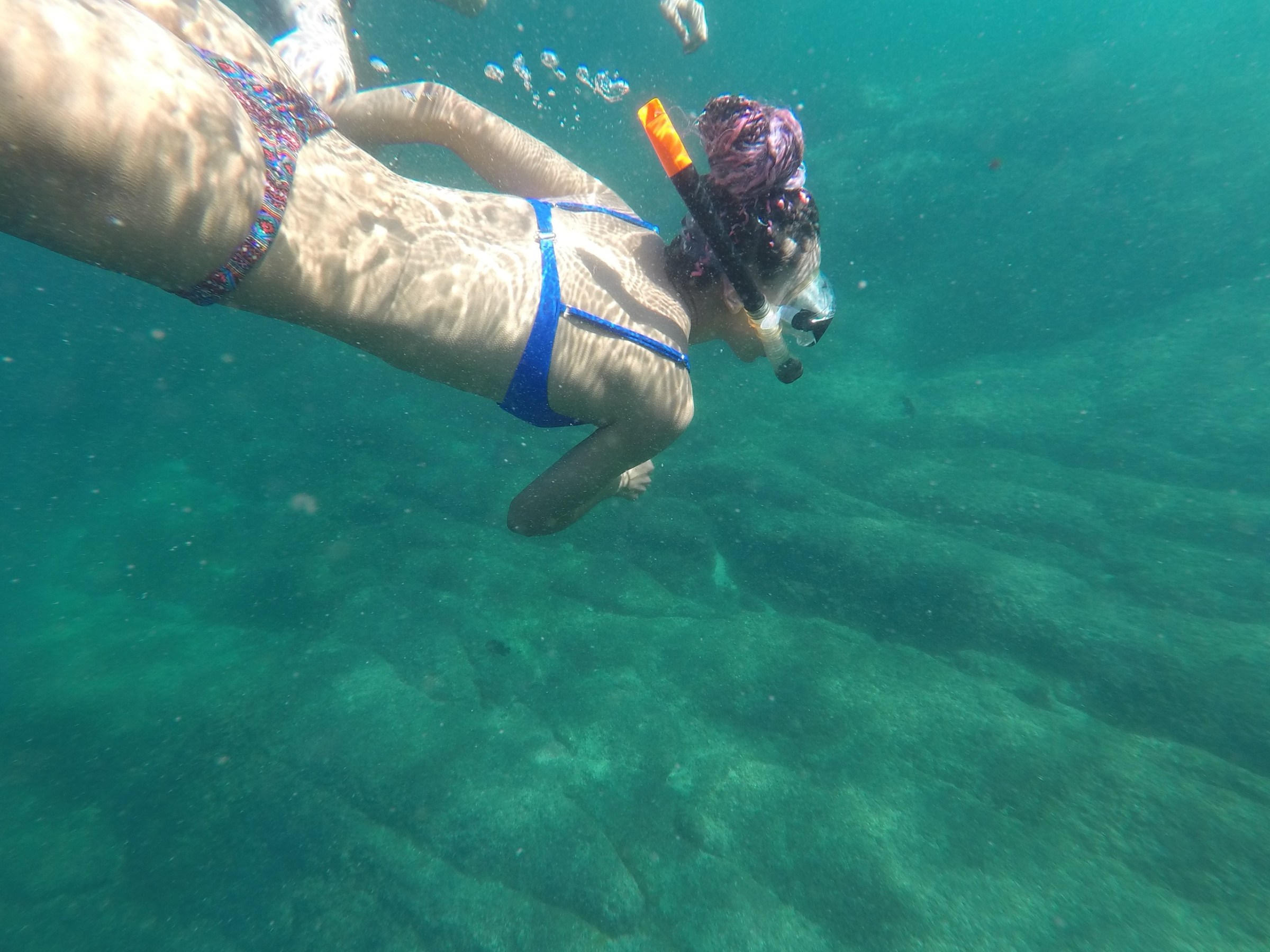 Person snorkeling underwater in clear blue-green sea.