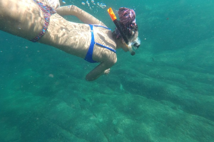 Person snorkeling underwater in clear blue-green sea.