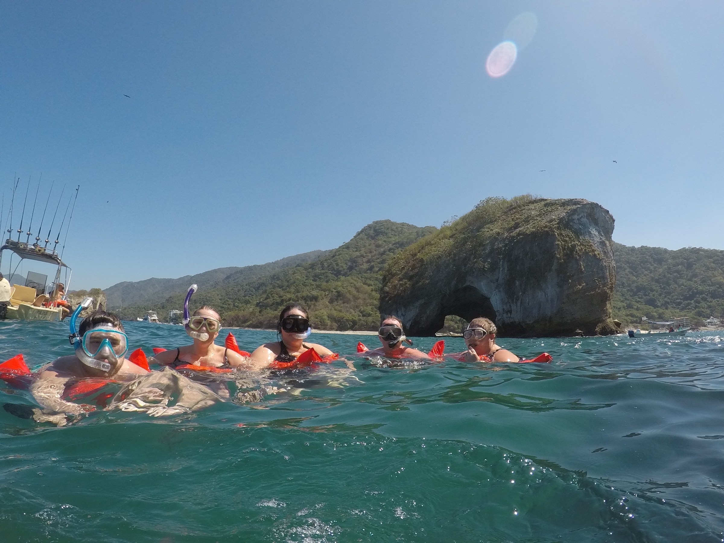 Five snorkelers in the ocean near a rocky island under a clear blue sky.