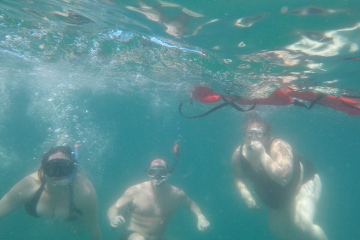 Three people snorkeling underwater with a red flotation device.