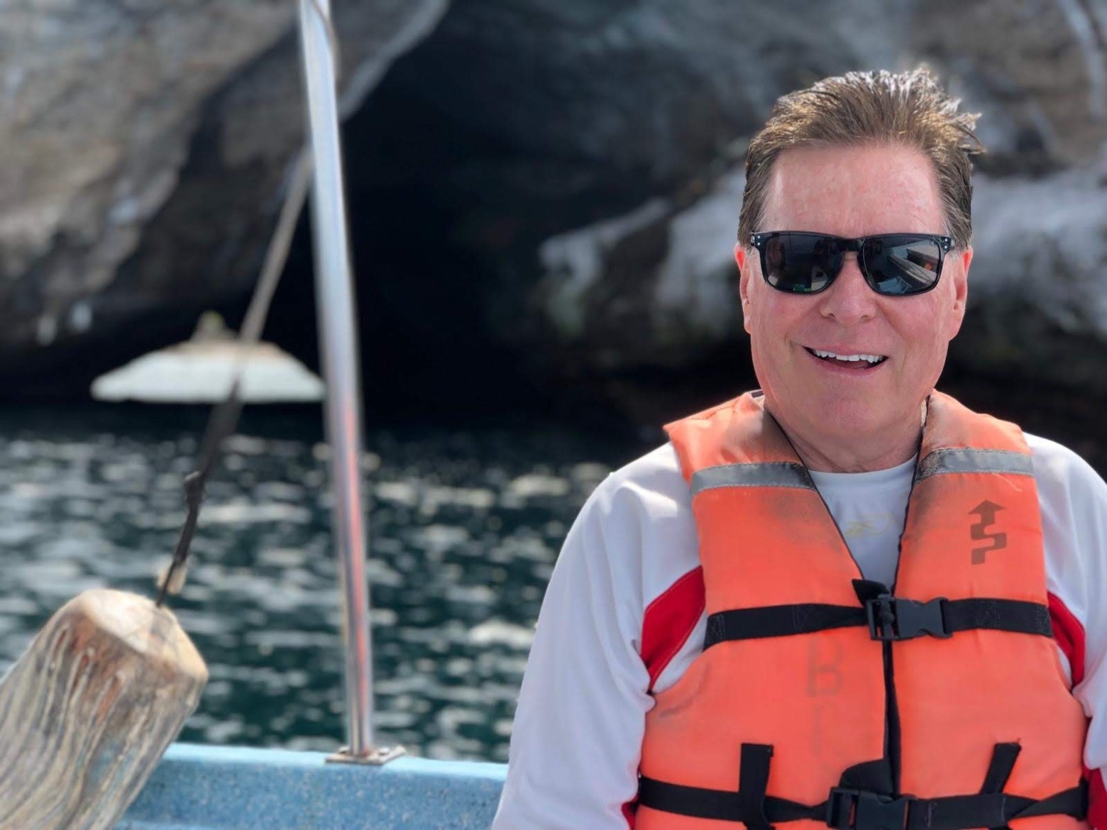 Man wearing sunglasses and life vest on a boat near a cave entrance.