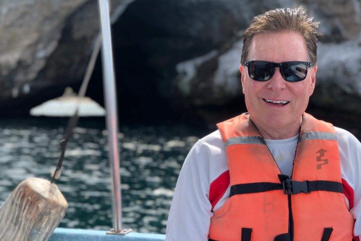 Man wearing sunglasses and life vest on a boat near a cave entrance.