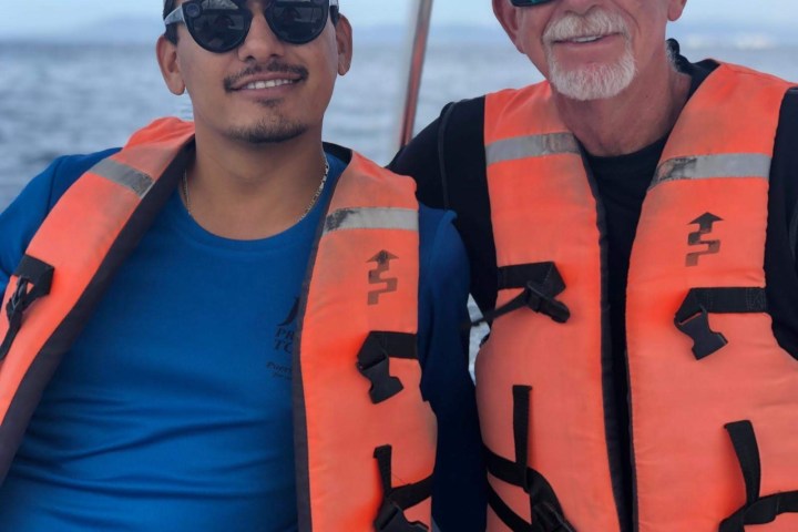 Two men wearing orange life vests on a boat with water in the background.
