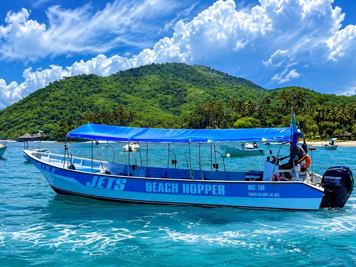 Blue boat named 'Beach Hopper' on water with lush green hills in background.