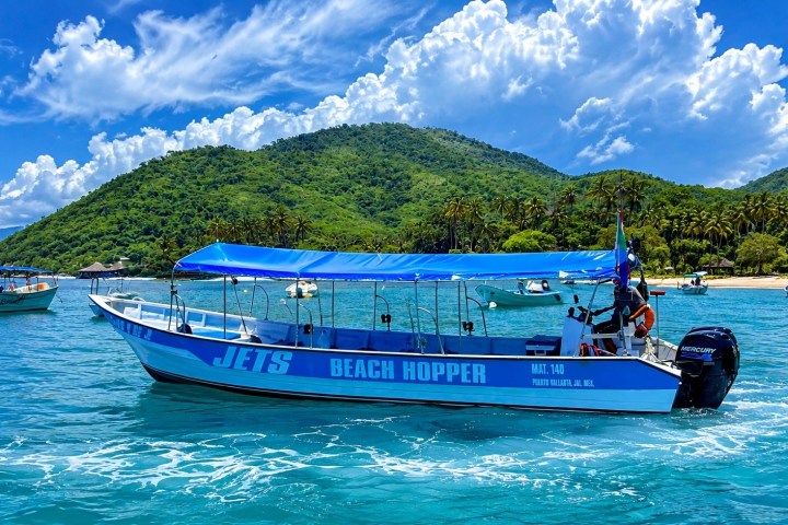 Blue boat named 'Beach Hopper' on water with lush green hills in background.