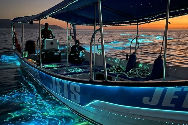 Boat on sea at sunset with glowing bioluminescent plankton in water.